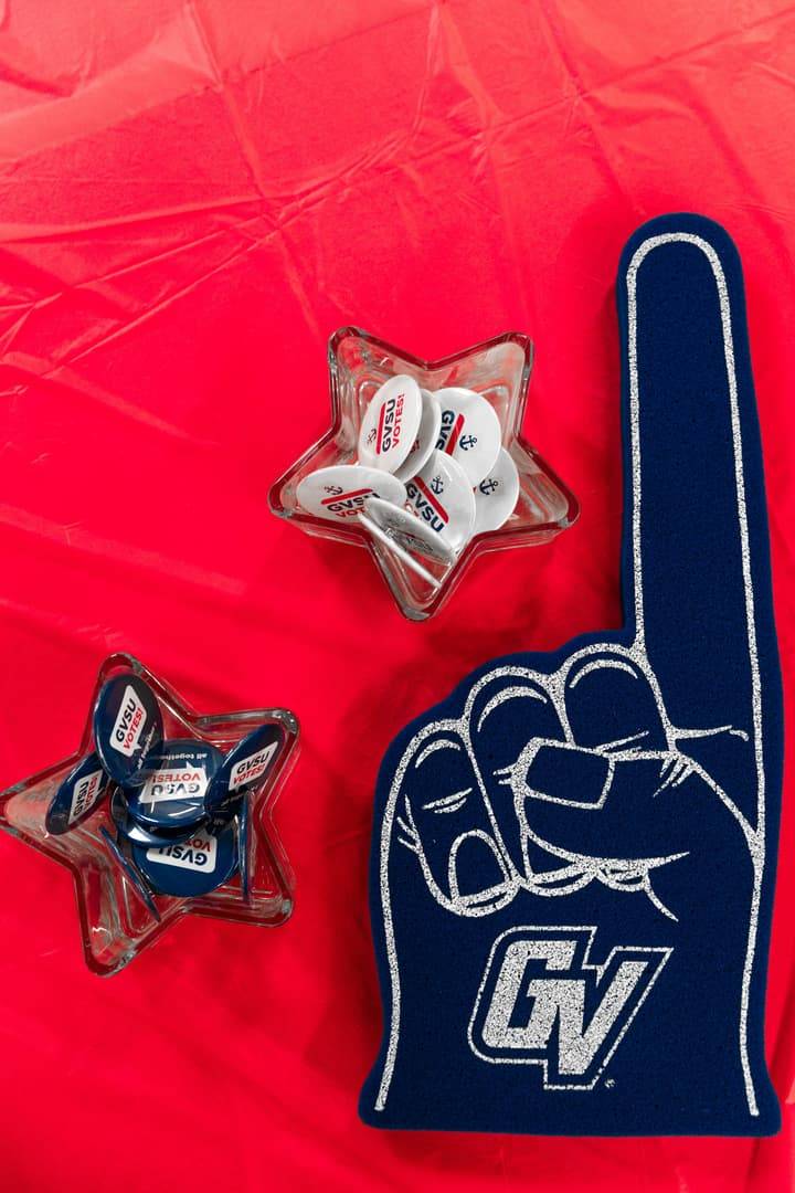 GVSU Votes Buttons & Foam Hand on Red Table